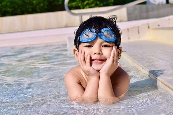 Enfant apprenant à nager dans une piscine avec des brassards pendant les vacances d'été.
